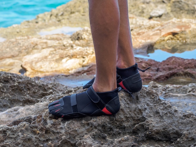 Crop A man in reef shoes is standing on a reef. sharp stones. near the ocean.