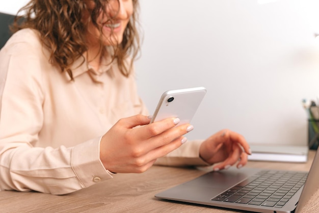 Crop photo of a young ecstatic woman using phone while working at laptop in the office