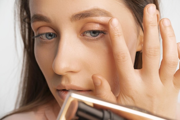 Crop photo of a young woman touching face while applying makeup