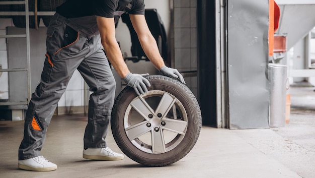 Photo crop portrait of full length mechanic holding tire at repair garage replacement of winter and summer tires