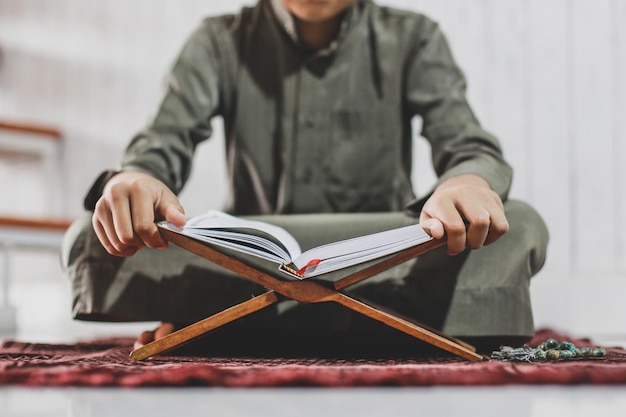 Photo crop shot of muslim boy reading the holy book alquran on the prayer mat with selective focus photo