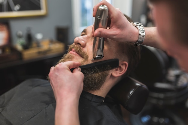 Crop stylist trimming beard of man