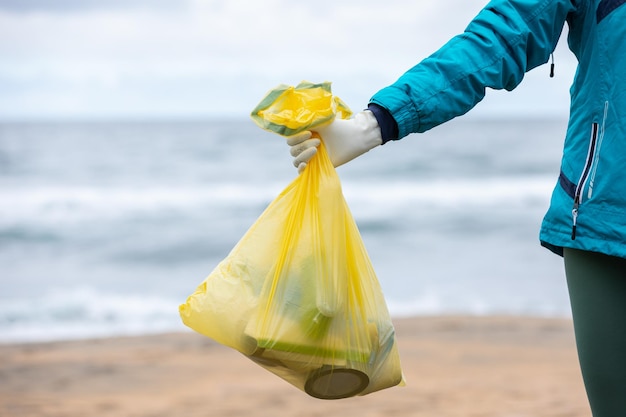 Crop unrecognizable female activist showing bag with collected garbage on seashore