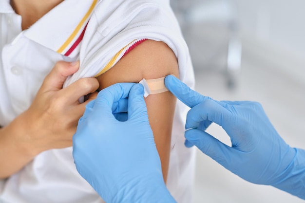 Crop unrecognizable nurse in disposable gloves applying medical patch on shoulder of patient in hospital