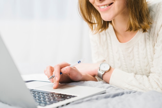 Crop woman browsing laptop on bed