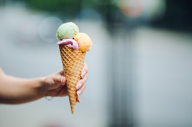 Crop of woman's hand holding delicious colorful ice cream with three colors Close up of tasty sweet mouthwatering perfect for summer heat while sunny day Summertime vibes and sweet food