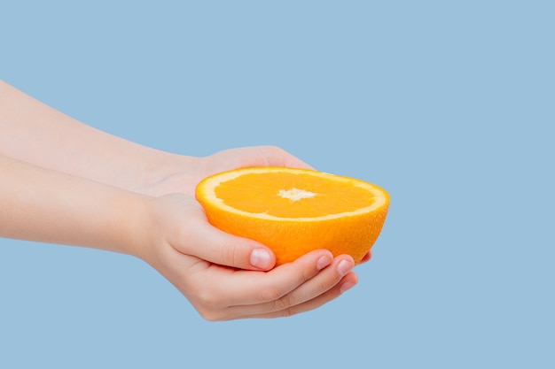 Croped half orange in the hands of girl isolated on blue