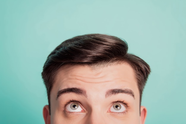 Cropped close-up portrait of curious guy look up empty blank space on teal background