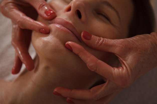 Cropped close up of a professional beautician doing face lifting massage for mature woman