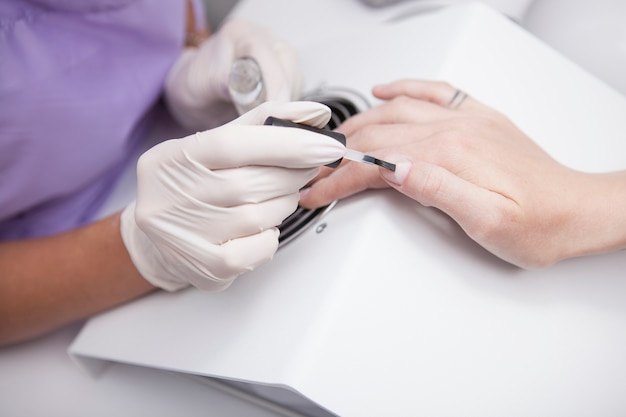 Cropped close up of professional manicurist preparing clients nails with base coat