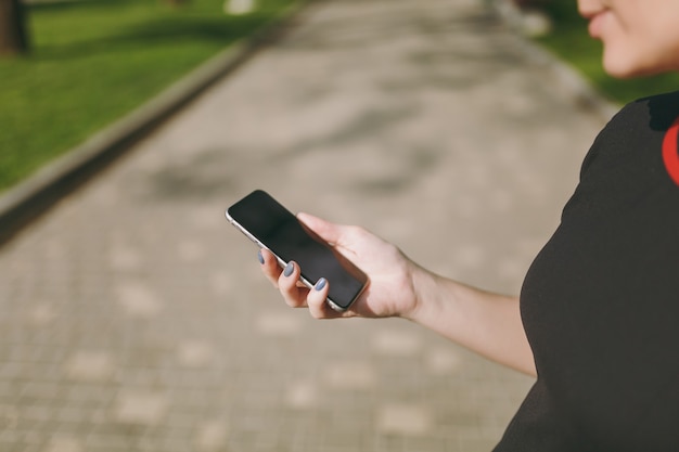 Cropped close up of woman hands holding and using mobile phone, smartphone with blank empty screen in city park outdoors