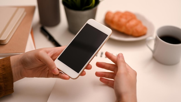 Cropped closeup image Female using smartphone to communicate with her friends at her office desk