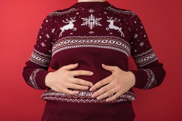 Cropped closeup photo of girl in red and white christmas sweater holding her hurting stomach on isolated red background