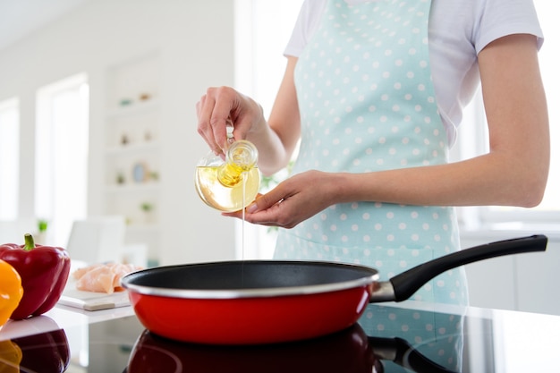 Cropped closeup photo of housewife hands holding olive oil bottle pouring warm frying pan weekend cooking tasty dinner preparation white light kitchen indoors