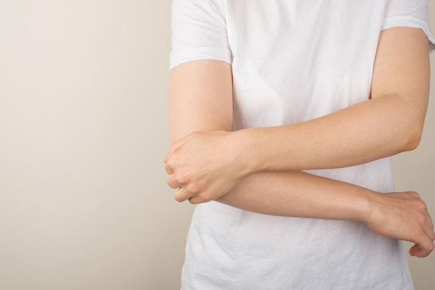 Cropped closeup photo of woman in white tshirt holding her right elbow on isolated grey background with copyspace