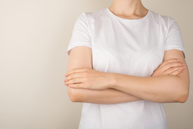 Cropped closeup photo of young woman in white tshirt with crossed arms on isolated grey background with empty space