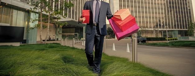 Cropped entrepreneur in suit holding shopping bag and giftbox outside the office reward