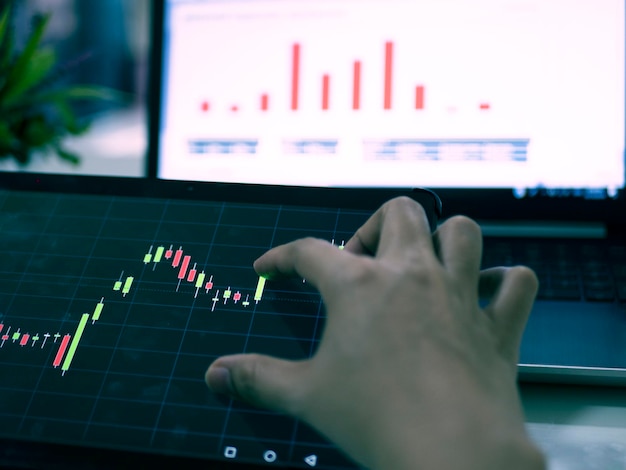 Photo cropped hand analyzing stock market data on digital tablet and laptop