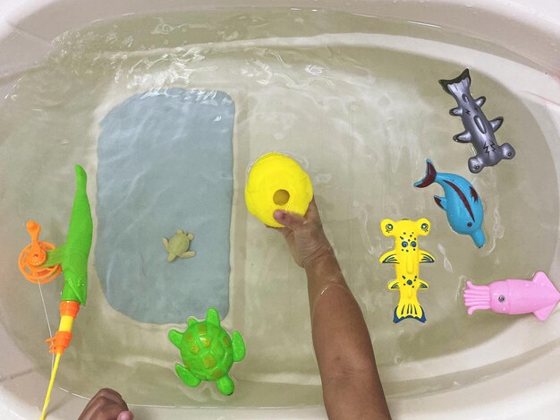 Cropped hand of child holding toys in bathtub