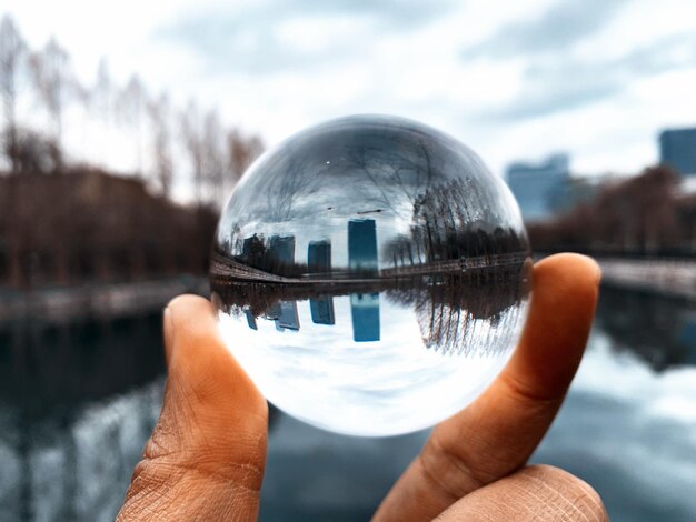 Photo cropped hand holding crystal ball with reflection of lake and buildings