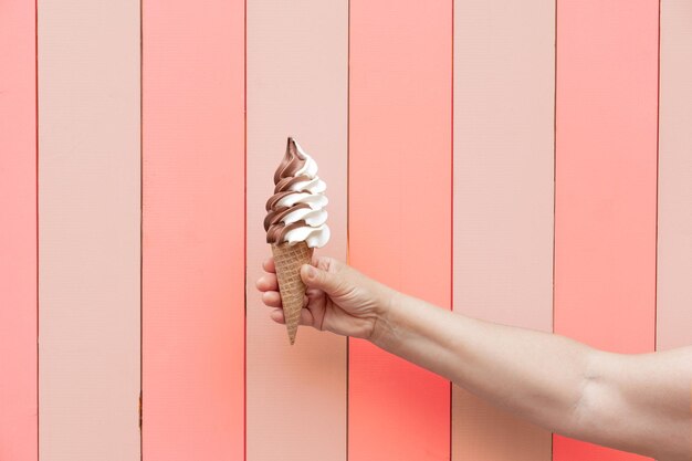 Cropped hand holding ice cream cone against wall