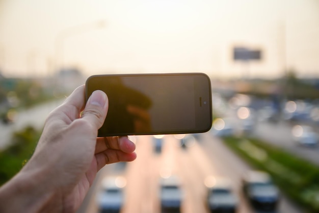 Photo cropped hand holding mobile phone with road in background