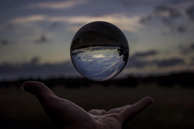 Photo cropped hand of man holding crystal ball in mid-air against sky during sunset