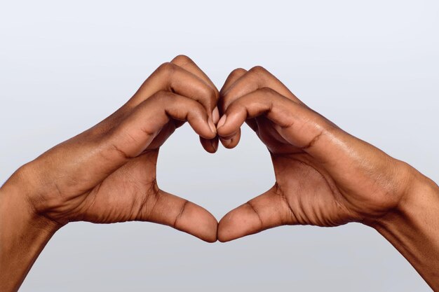 Cropped hand of person gesturing heart shape against white background