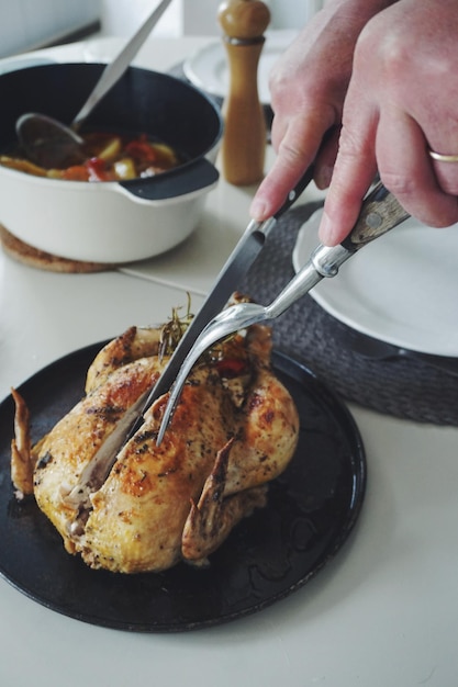 Photo cropped hand of woman cutting roasted chicken in plate