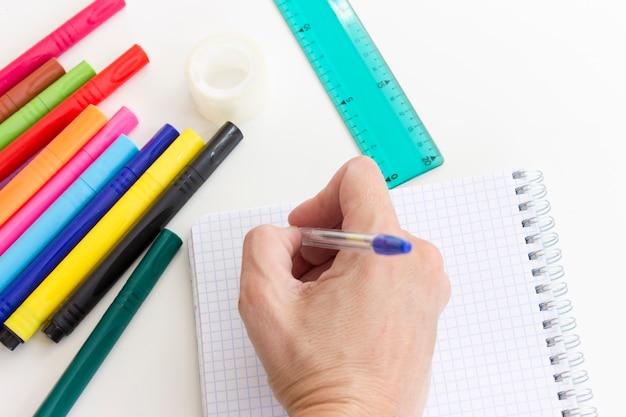 Cropped hand writing in notebook. Multi Colored marker pens, notebook, ruler on white. 