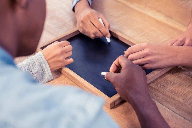 Cropped hands of business people writing on slate at desk in creative office