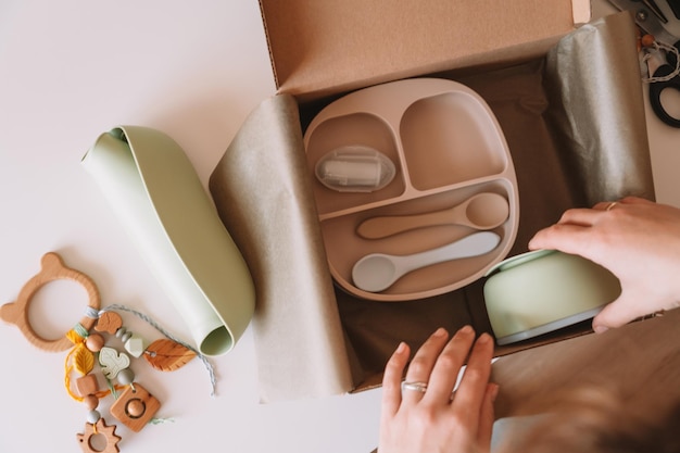 Cropped hands packing wrapping shipment with silicone baby dishes plate spoons bowl eco teether in box Top view