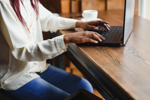 Cropped image of Afro American girl drinking coffee while working with a laptop in cafe