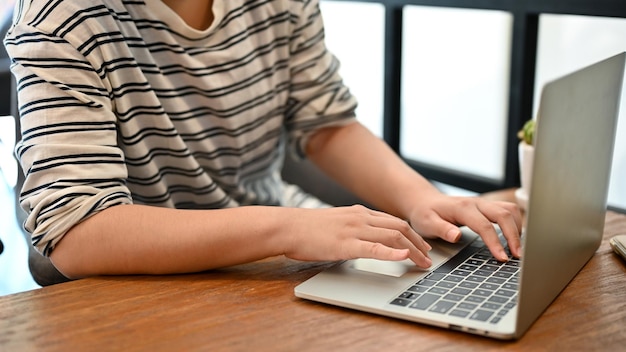 Cropped image of an Asian girl in casual clothes using her laptop computer