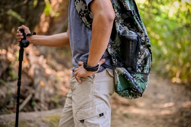 Cropped image of an Asian male traveler with backpack and trekking gear stands in the forest