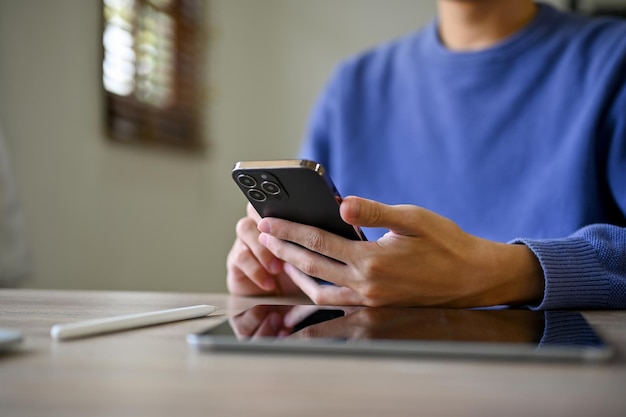 Cropped image of an Asian man using his smartphone at his desk text chat message