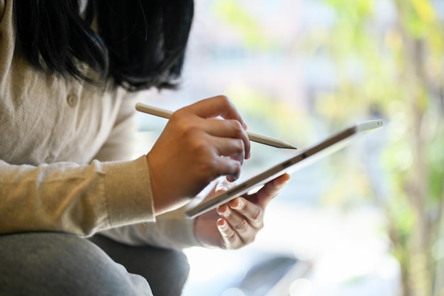 Cropped image of an Asian woman holding stylus pen using digital tablet working on her project