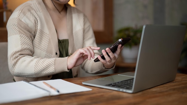 Cropped image of an Asian woman using her smartphone while working remotely at a coffee shop