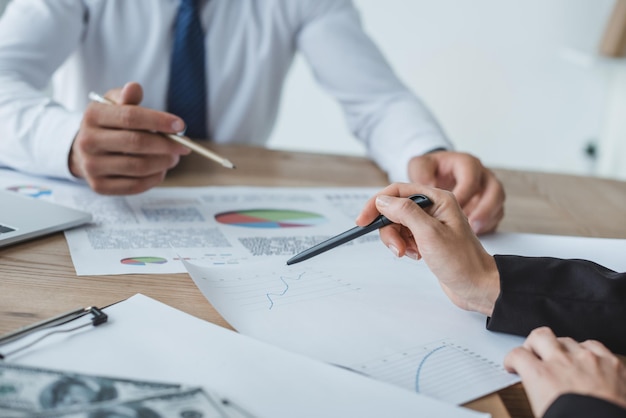 Cropped image of business advisers pointing on documents at table in office