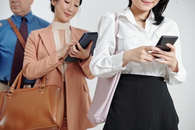 Cropped image of business people standing in queue and using mobile applications on smartphones