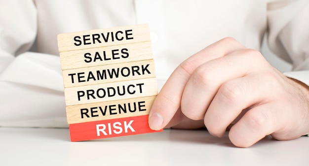 Cropped image of businessman holding red risk block under wooden tower at table