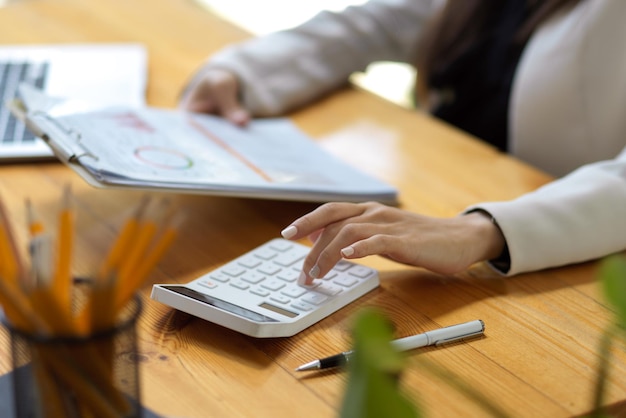 Cropped image of a businesswoman, female accountant using calculator and examining financial report.