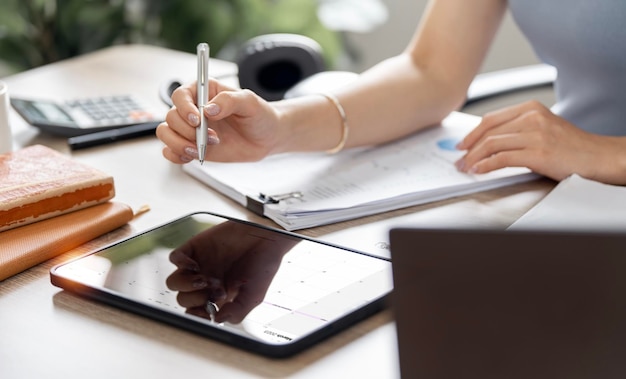 Cropped image of businesswoman hand analyzing weekly schedule in her tablet sitting at her desk office