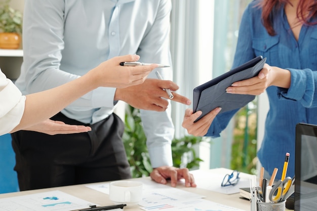 Cropped image of businesswoman showing report on digital tablet to colleagues at meeting