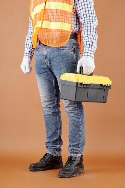 Cropped image of carpenter in jeans and bright vest holding toolbox