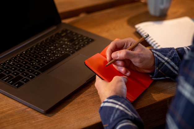 Cropped image of casual business man or freelancer planning his work on notebook working on laptop c...