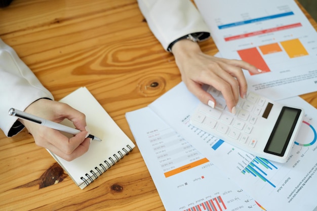 Cropped image of a female accountant or consultant using calculator and taking notes on notepad