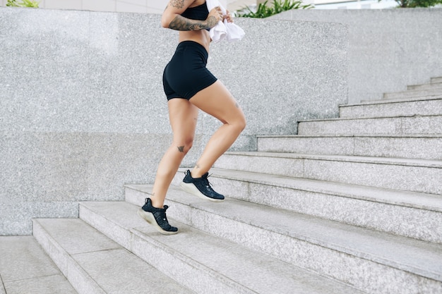 Cropped image of fit young woman with towel in hands running up the stairs