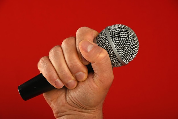 Cropped image of hand holding microphone against red background