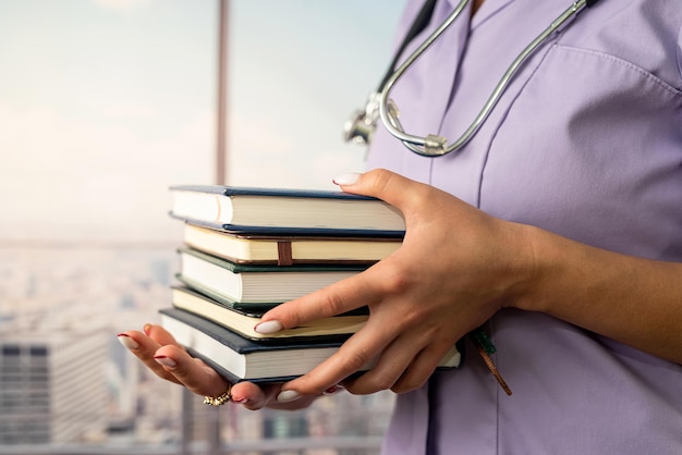 Cropped image of intern in med uniform holding many books in front of her in hospital